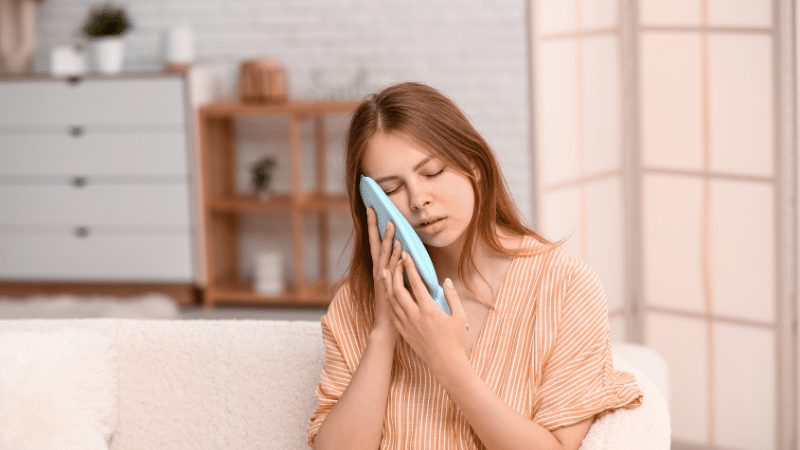 Woman holding ice pack to her cheek for tooth pain relief after root canal treatment.