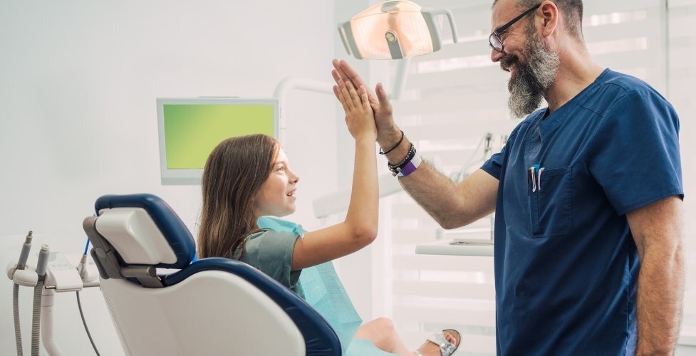 Pediatric dentist high-fiving young patient in dental chair to build confidence.