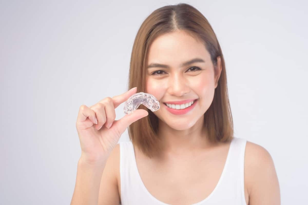 Woman holding clear Invisalign aligner, smiling to show teeth straightening results.