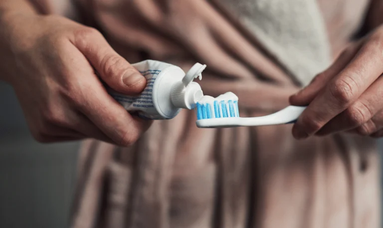 Hands squeezing toothpaste onto a toothbrush