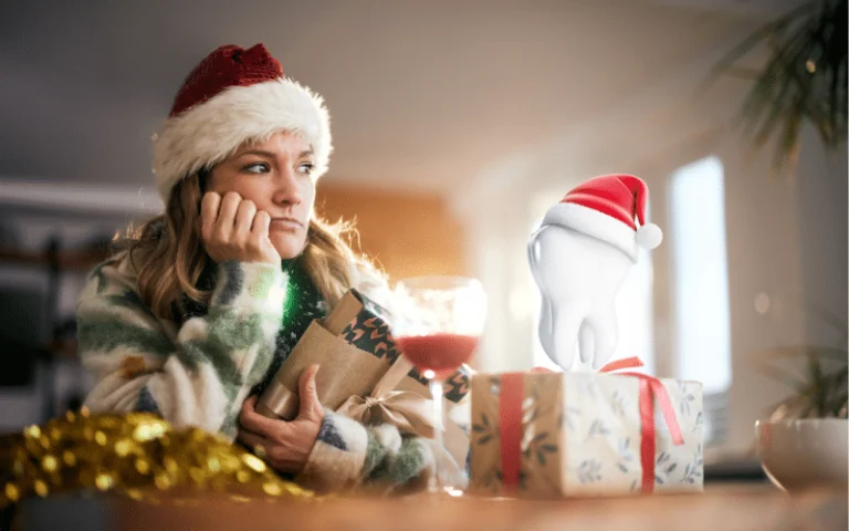 Woman in a Santa hat holding her cheek beside holiday gifts
