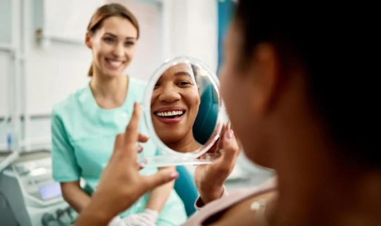 Patient looking at her smile in a mirror held by a smiling dental assistant