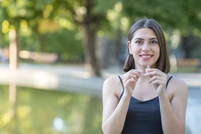 Woman holding a clear aligner outdoors by a pond